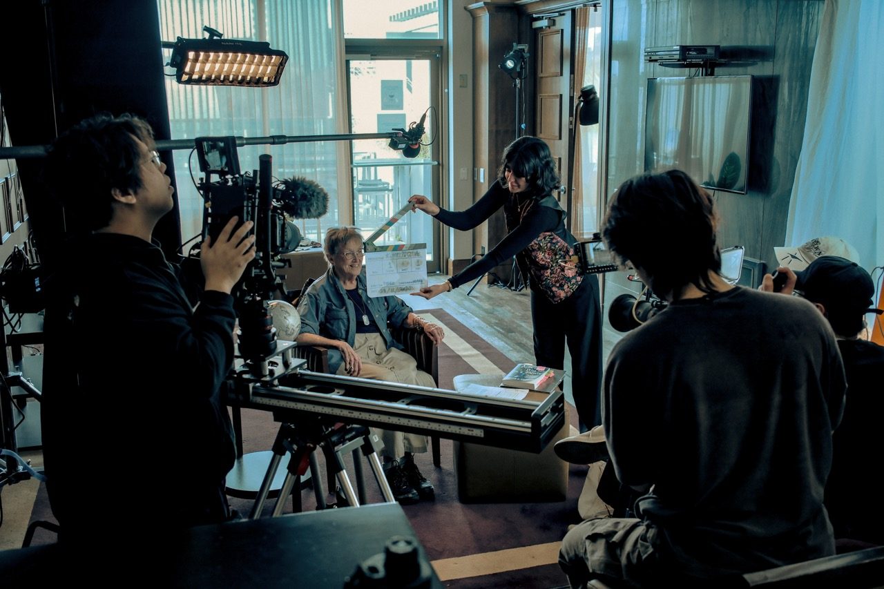Deniz holding the slate on set as the crew films Joyce Perrin