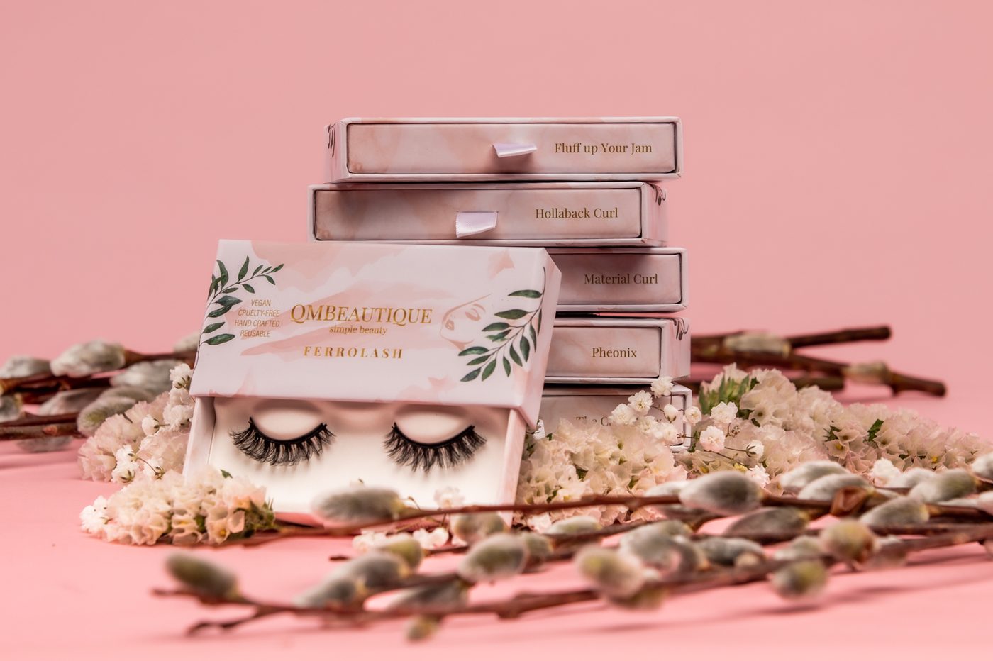 A stack of Ferrolash lash boxes named Fluff Up Your Jam, Hollaback Curl, Material Curl and Pheonix, with one open box in front, surrounded by flowers and pussy willow