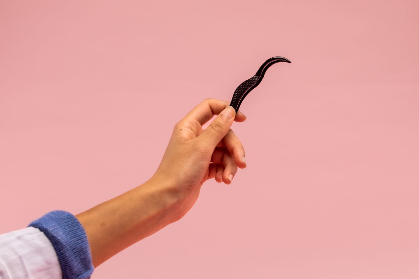 Lash applicator tweezers held up against pink