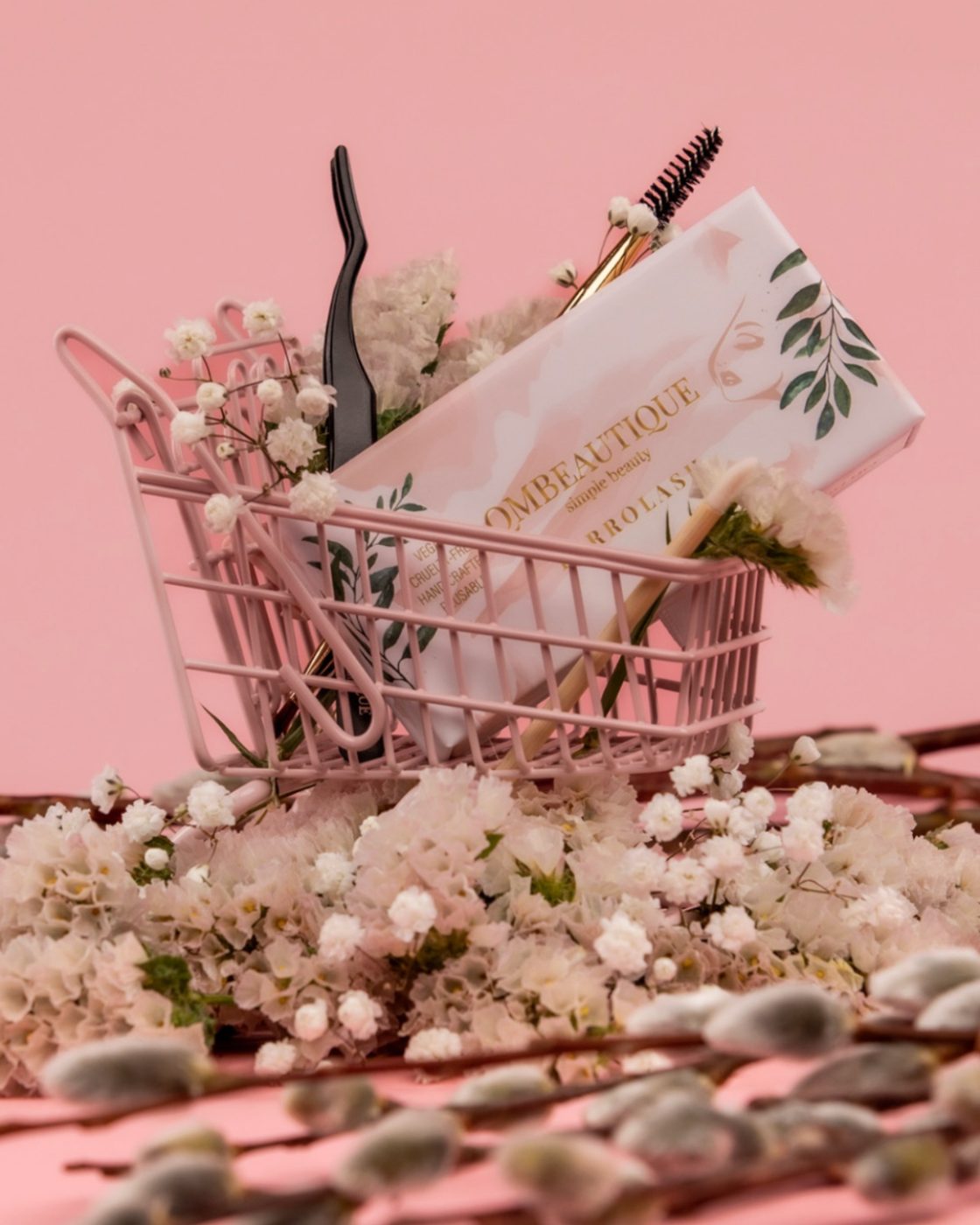 A pink mini shopping cart full of lash boxes, tweezers and flowers