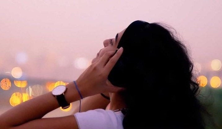 She tilts her head back at dusk, city lights blurred behind her