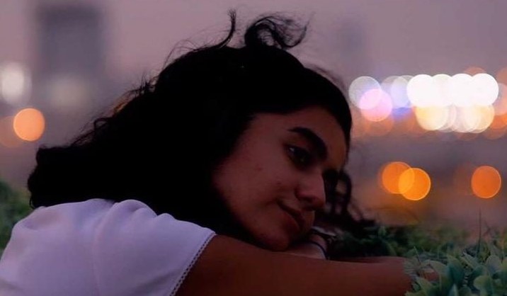 She rests her head on her arms, smiling, against bokeh city lights